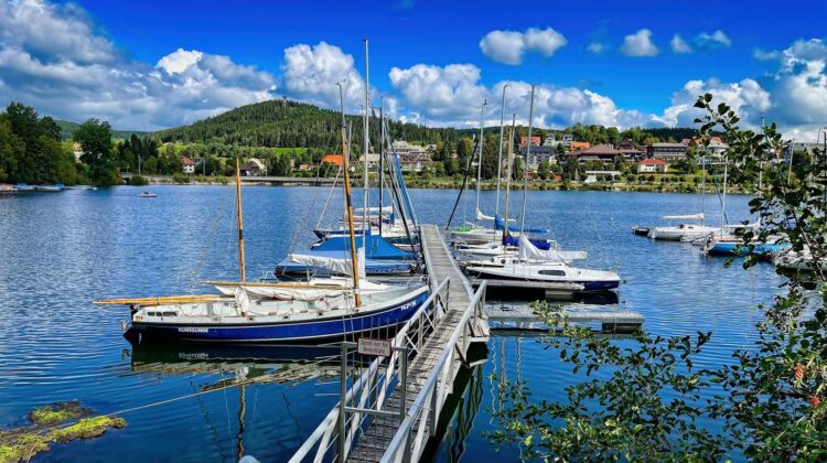 Segelboote am Steg im Hafen des Schluchsees im Südschwarzwald, dahinter der bewaldete Ort